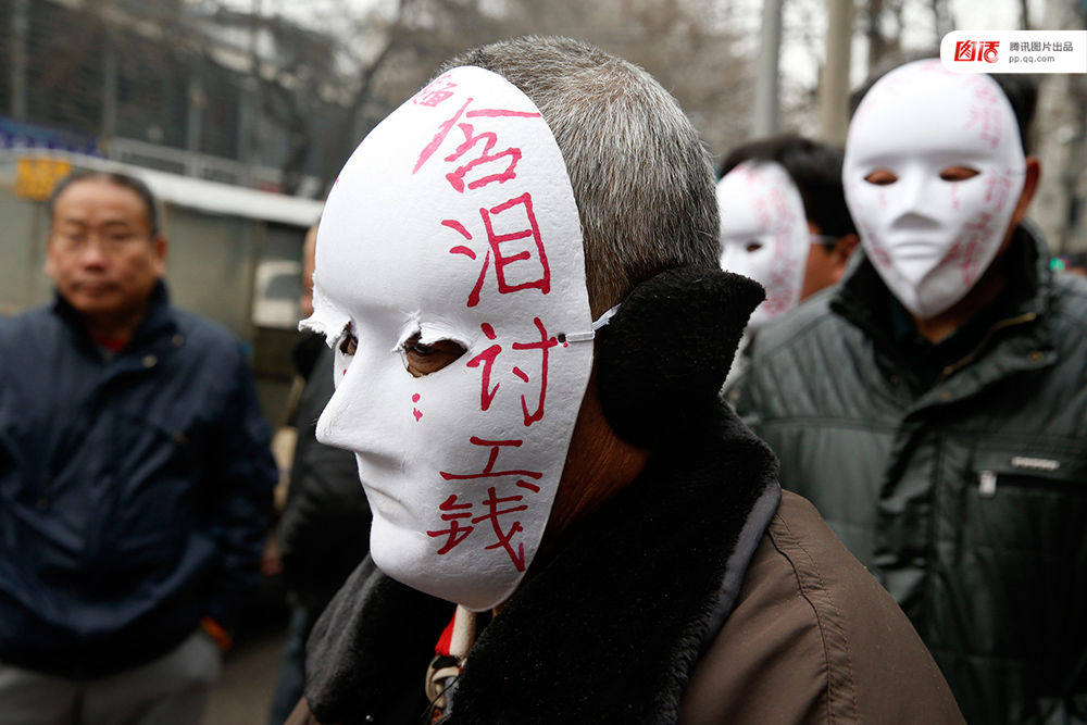 近几年，由于经济增速下行，中西部地区和中小城市成为当前讨薪矛盾多发地区。一边是国家和地方维护打工者权益的法律法规不断出台，另一边则是“年年干活年年欠，年年讨薪年年难”。不少打工者不得已只好采取行为艺术等手段以博取关注。图为2015年2月2日，西安市尚德路陕西省水利厅的门前，七八位头戴着白色面具者站在凛凛寒风中，面具上写着：“含泪讨工钱” “无颜见父母”等标语。据了解，这几个人是70名农民工的代表，他们之前在武功县干的工程被欠款156万元。谁知，包工头不但电话打不通，以前的家也搬了，根本找不到人，多次找到水