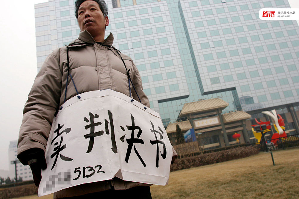 2006年1月24日，在京从事降水井工程的老陈挂着写有“卖判决书”的纸口袋在北京站口附近来回走着。曾是名小工头的老陈被欠工程款4万元，为了给工人们开资不得已卖掉了打井机器。2002年法院宣判老陈胜诉，可四年后该判决仍得不到执行，无奈之中老陈只好上演此幕。程宁/视觉中国
