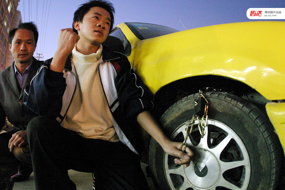 2004年12月6日下午，福建泉州，因一家面临停产的服装加工厂，拖欠15名工人3个月工资及1个月押金，工人声称没有钱吃饭了，10多名工人只好集资12元买来一条铁链锁，把老板的轿车前轮锁住。记者获悉前往采访，老板看到记者到来，从车间后面一“秘密通道”（平时铁门紧锁的消防通道）开溜。随后，记者与老板通上电话，老板称没有拖欠3个月工资，而是1个月。小洪/视觉中国
